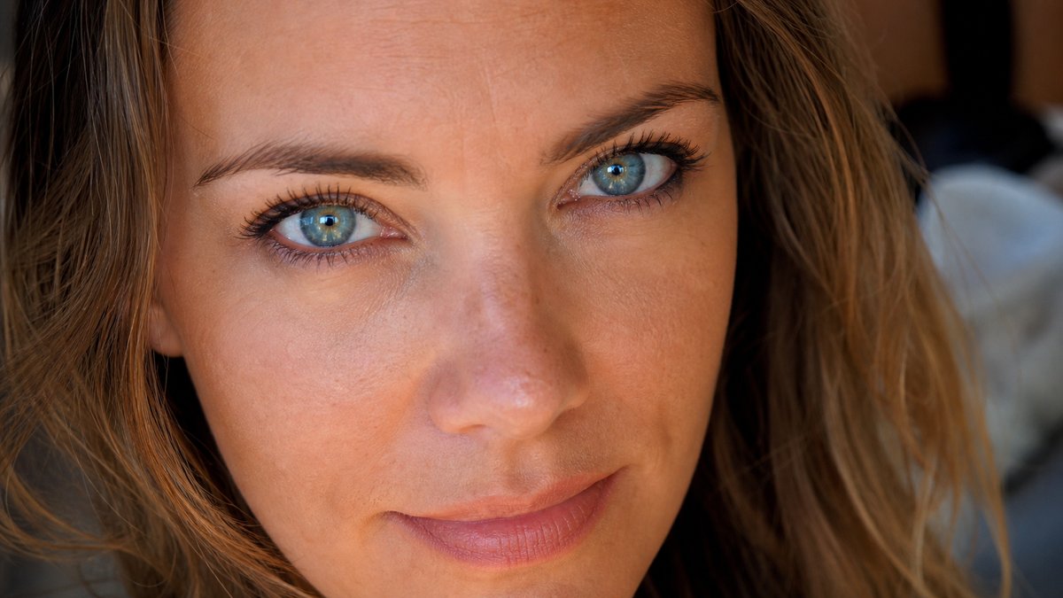 Close-up portret van een vrouw met intense blauwgroene ogen en warm goudbruin haar, lichtgevende teint