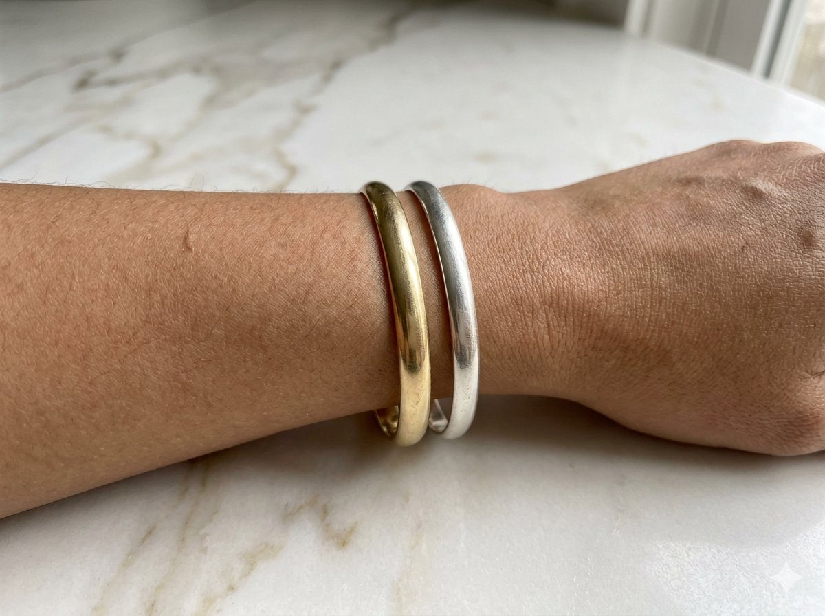 Pols met een gouden armband en een zilveren armband naast elkaar om hun effect op de huidtint te vergelijken